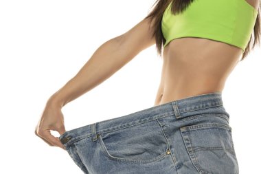 Diet concept and weight loss. Woman in oversize jeans on white background. Close up.
