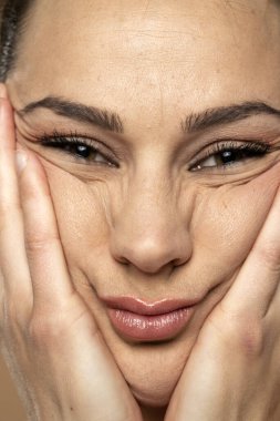A young woman crumples the skin of her face with her hands. Close up.
