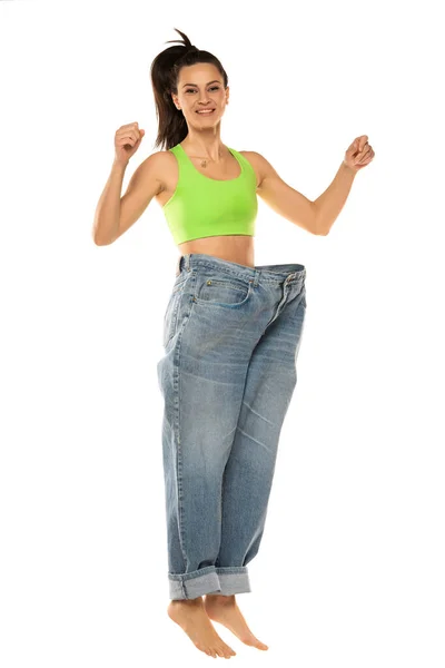 国会の概念と減量 白い背景を飛び越えるオーバーサイズのジーンズの幸せな女性 閉じろ — ストック写真