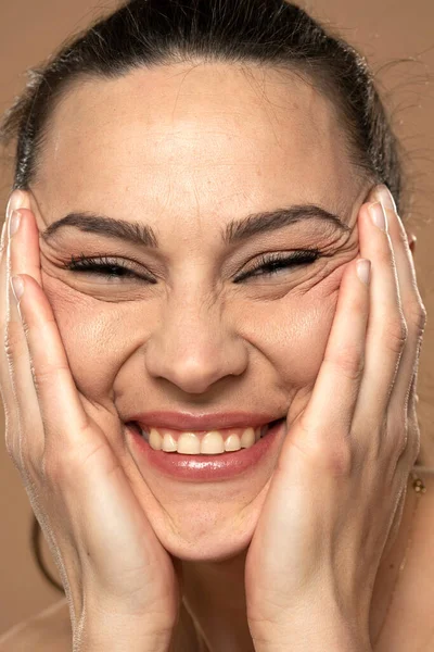 A young smiling woman crumples the skin of her face with her hands. Close up.
