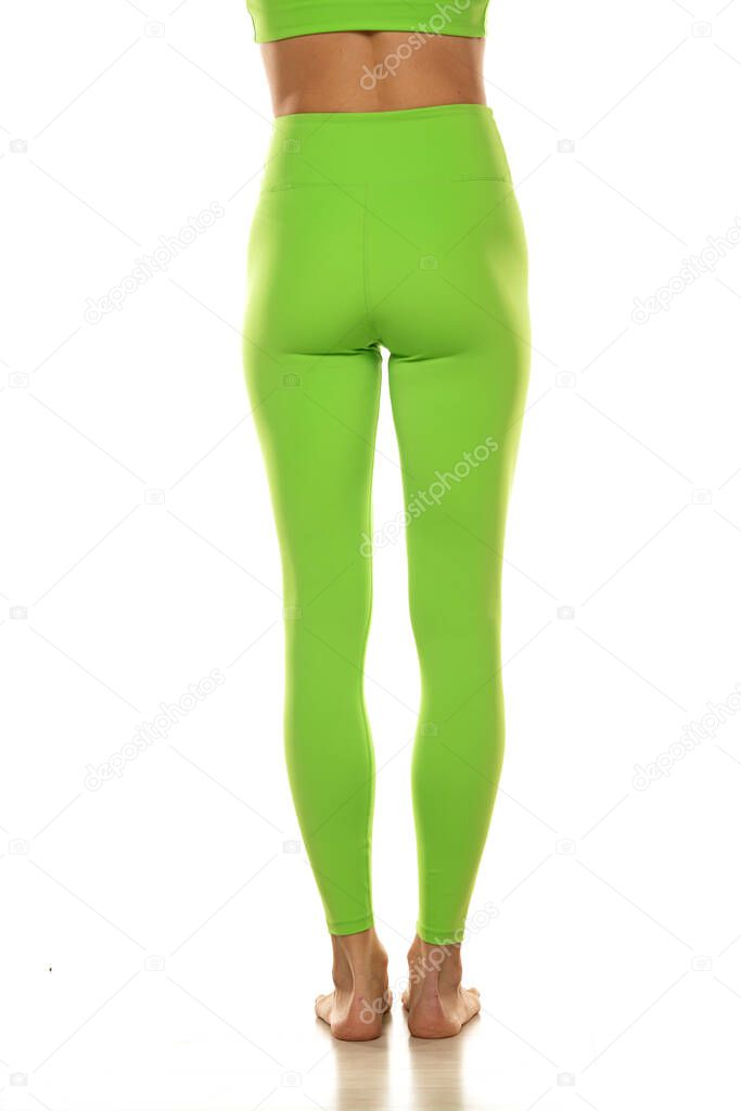 Sporty green leggings on slim pretty bare legs on a white background. Rear view.