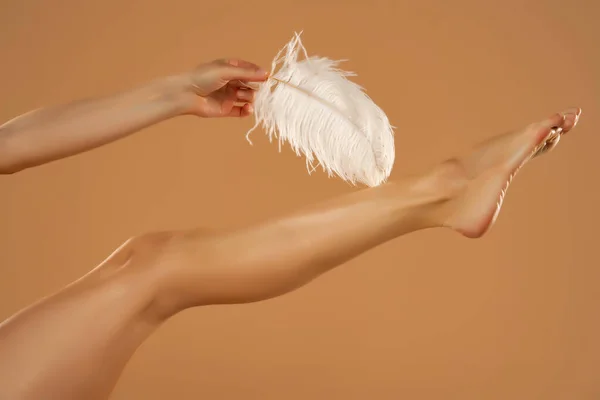 年轻女子的手触摸她的腿与白色羽毛米色背景 美丽的身体护理理念 — 图库照片