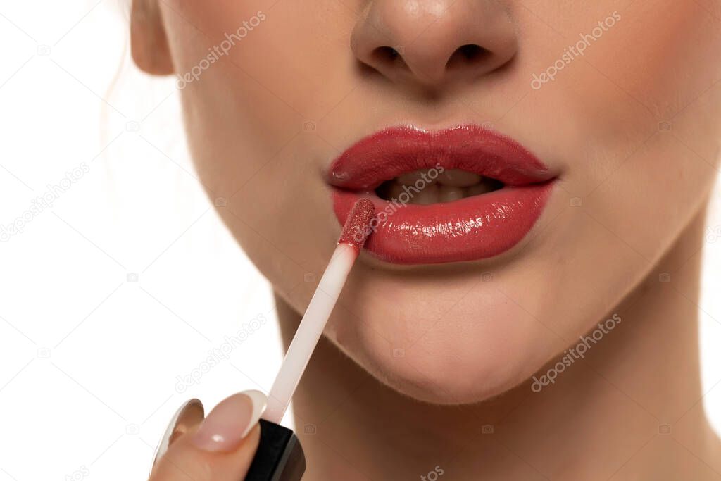 young beautiful woman apply a lip gloss on her lips on white background.