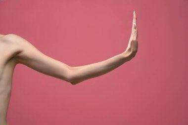 Genç bayanın sıska kolu hareketsiz duruyor. Pembe arka planda izole edilmiş.