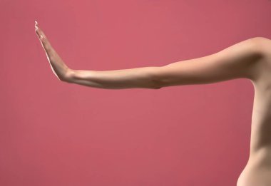Genç bayanın sıska kolu hareketsiz duruyor. Pembe arka planda izole edilmiş.