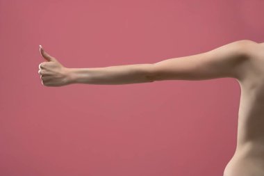 Genç kadının sıska baş parmağı yukarıda. Pembe arka planda izole edilmiş.