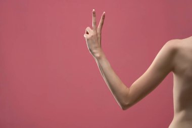 Genç bir kadının kolu iki parmağını gösteriyor. Pembe arka planda izole edilmiş.