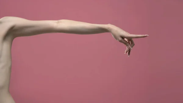 Young woman\'s stretched skinny arm and touching imaginary product with index finger. Isolated on pink background.