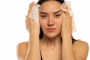 Beyaz arka planda ıslak mendille yüzünü temizleyen genç bir kadın.