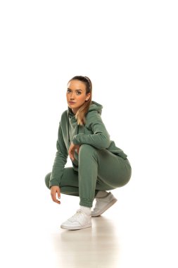 Portrait of a young woman in sports clothes, kneeling and posing, against studio white background.