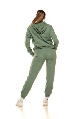 Arka planda yeşil eşofmanlı genç bir kadın stüdyoda beyaz bir arka plana poz veriyor..