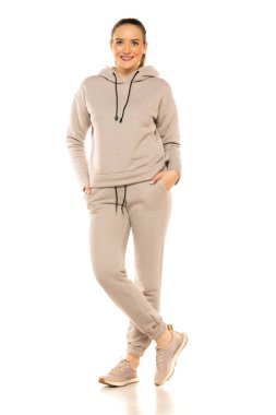 Gri eşofmanlı gülümseyen genç bir kadının stüdyoda beyaz bir arka plana poz verişi..