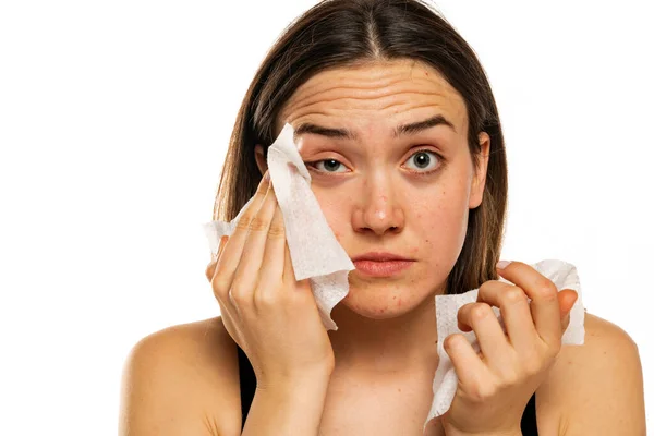 年轻的女人在白色的背景上用湿巾擦拭她的脸 — 图库照片