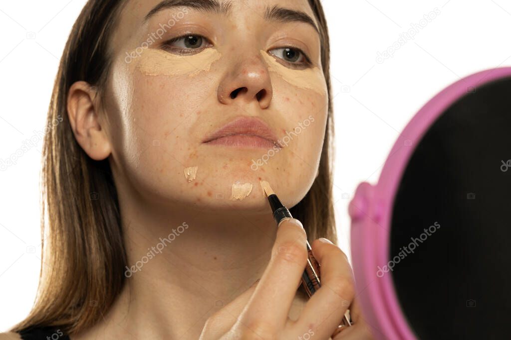 Young women applying concealer under her eyes and face on white background