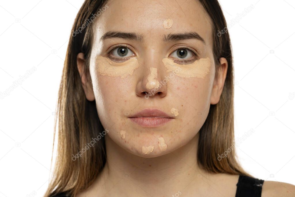 Young women posing with concealer under her eyes and face on white background