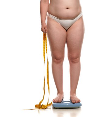obesity and overweight, overweight woman legs and belly on the scale, holding mettering tape. concept of obesity.