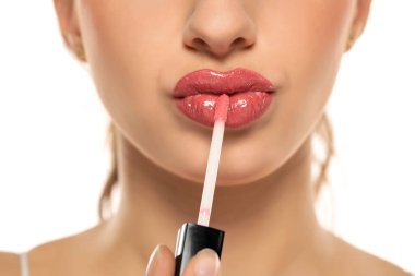 Close up of beautiful young woman applying lipgloss on a white background.