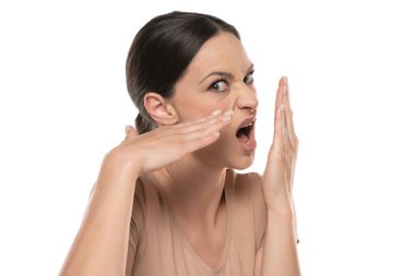 Profile of a young frowning woman checks her breath with her palm on a white background.