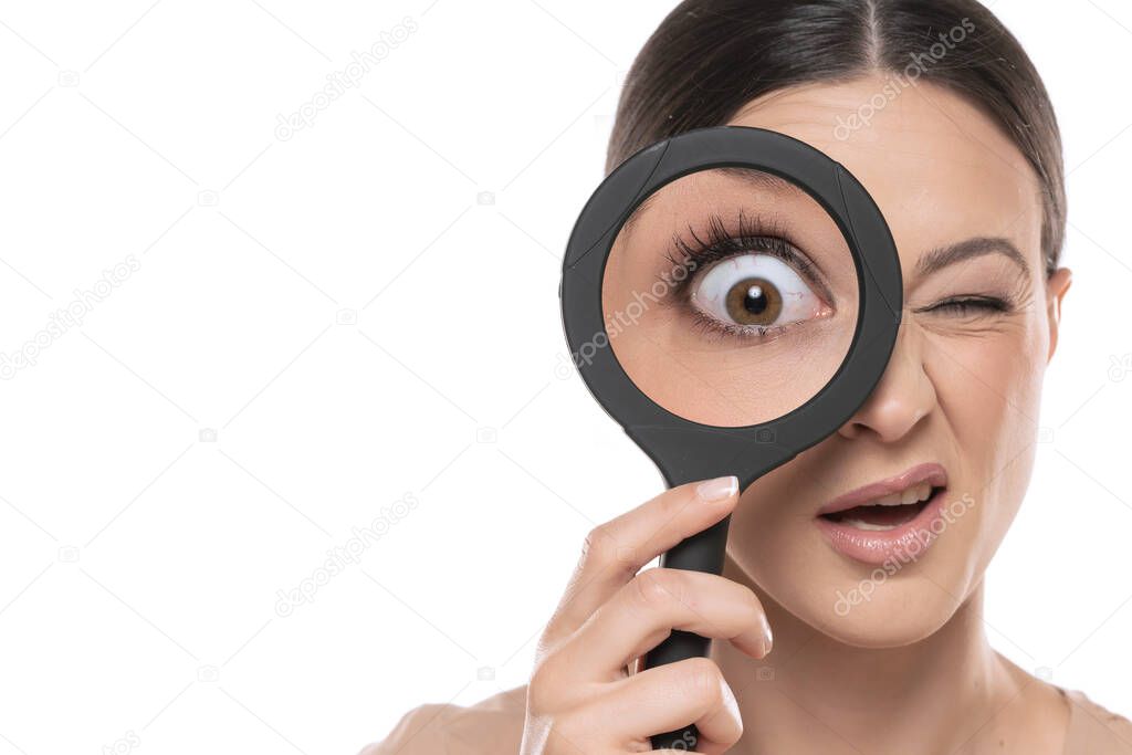 Close-up portrait of young woman looking through a magnifying glass on a white studio background.