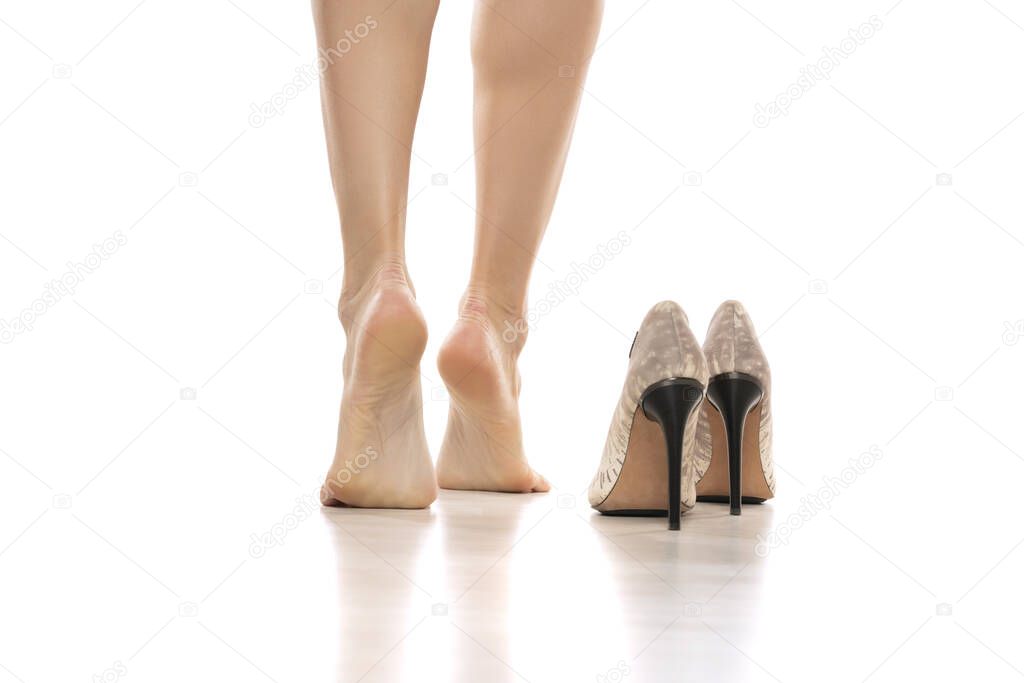 Back view of a woman's bare feet and high heels on a white studio background.