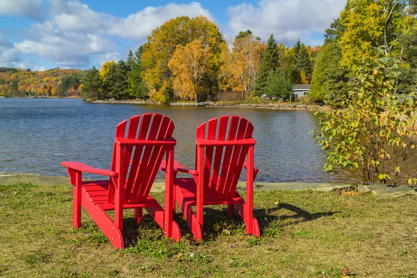Sedie Adirondack rosse su una riva del lago Immagine Stock