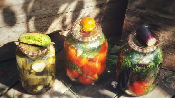 Three canned jars with vegetables in the country house, in the cellar, cucumber, eggplant and tomato on the lids. Canned vegetables.fresh lemonade with lemon and mint