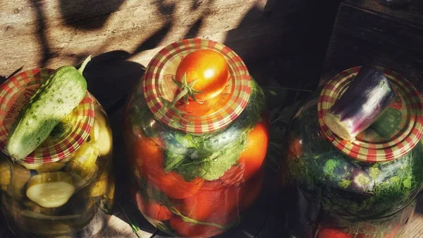 Three canned jars with vegetables in the country house, in the cellar, cucumber, eggplant and tomato on the lids. Canned vegetables.fresh lemonade with lemon and mint