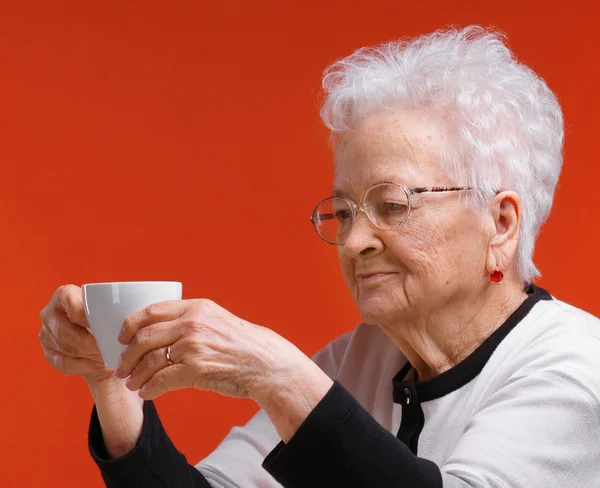 Oude vrouw in glazen genieten van koffie of thee — Stockfoto