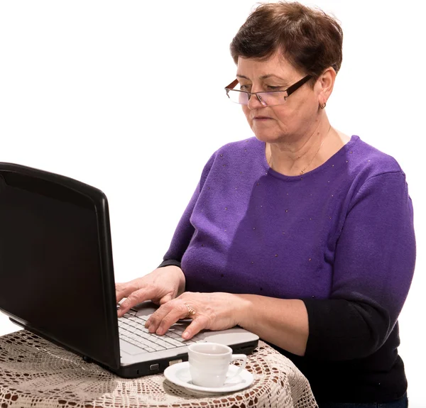 Volwassen vrouw in glazen werken op de computer met kop koffie — Stockfoto