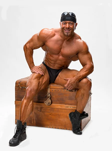 Bodybuilder sitting on a wooden chest — Stock Photo, Image