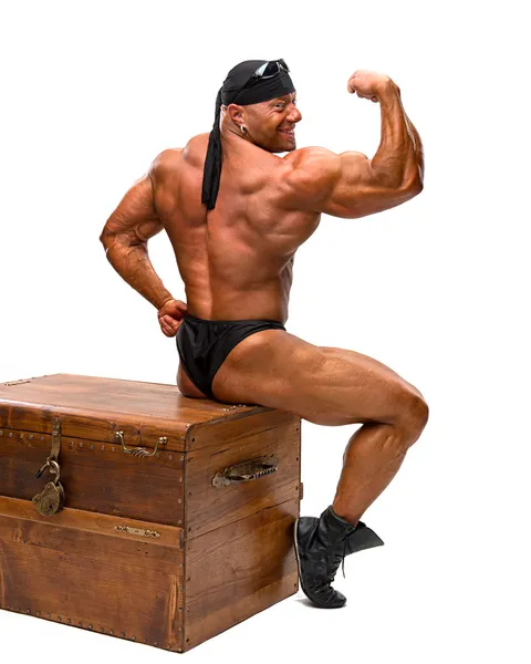 Bodybuilder sitting on a wooden chest — Stock Photo, Image