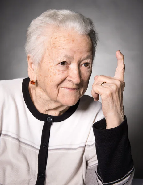 Portrait of a happy old woman pointing upwards — Stock Photo, Image