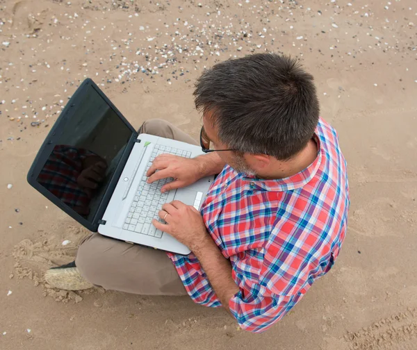 Homme d'affaires âgé assis avec ordinateur portable sur la plage — Photo