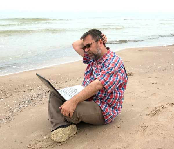 Homme d'affaires âgé assis avec ordinateur portable sur la plage — Photo