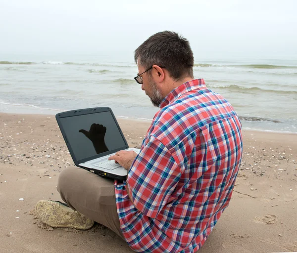 Äldre affärsmannen sitter med anteckningsboken på stranden — Stockfoto