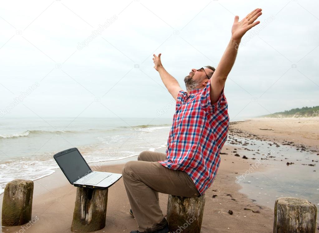 Emotional businessman with laptop on the beach