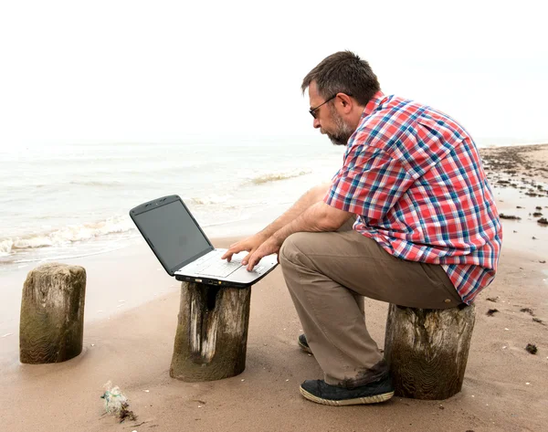 Äldre affärsmannen sitter med anteckningsboken på stranden — Stockfoto