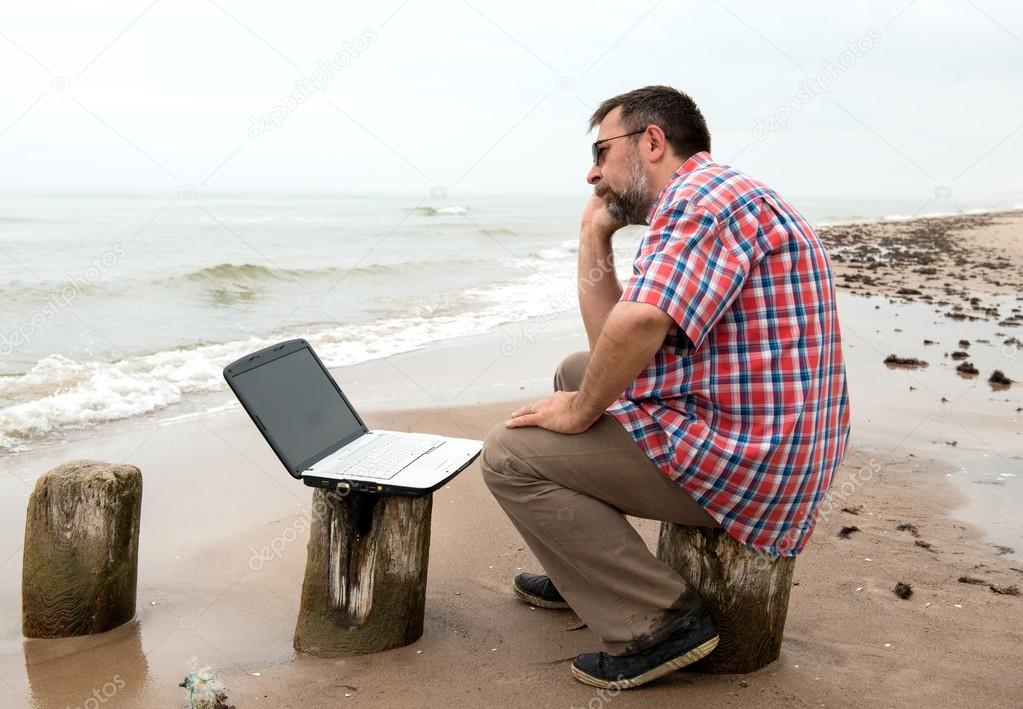 Tired businessman sitting with notebook on beach