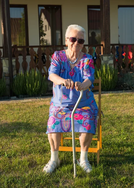 Vieille femme assise sur une chaise avec une canne — Photo