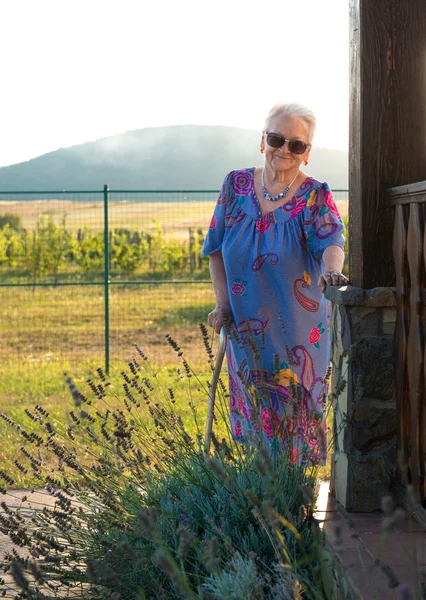 Old woman in sunglasses standing with a cane — Stock Photo, Image