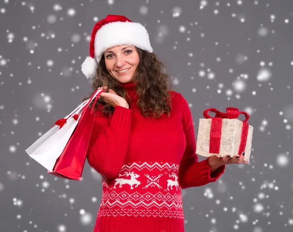 Mujer sonriente en sombrero de santa con bolsas de compras y caja de regalo — Foto de Stock