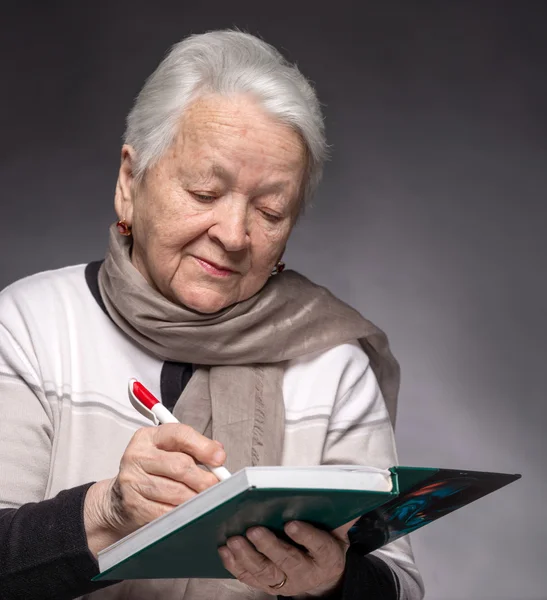 Старшая женщина пишет заметки в блокноте — стоковое фото
