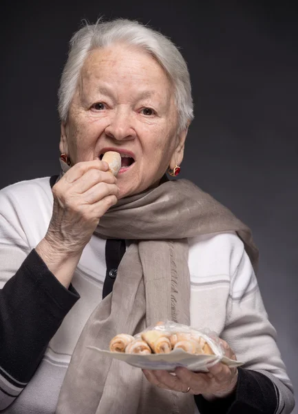 Old woman tasting cookies — Stock Photo, Image