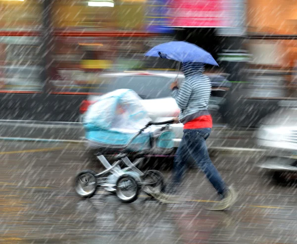 母は、雨の日にベビーカーで子供と歩く — ストック写真