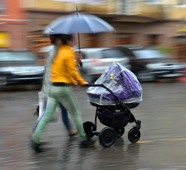 母は、雨の日にベビーカーで子供と歩く — ストック写真