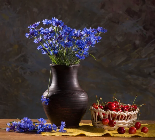 Flores de maíz azules en jarrón y cerezas — Foto de Stock