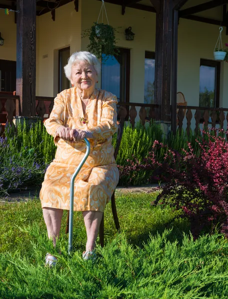 Gammal kvinna sitter på en stol med käpp — Stockfoto