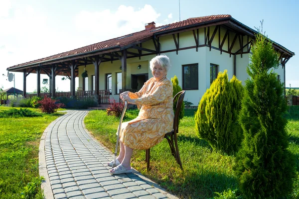 Gammal kvinna sitter på en stol med käpp — Stockfoto