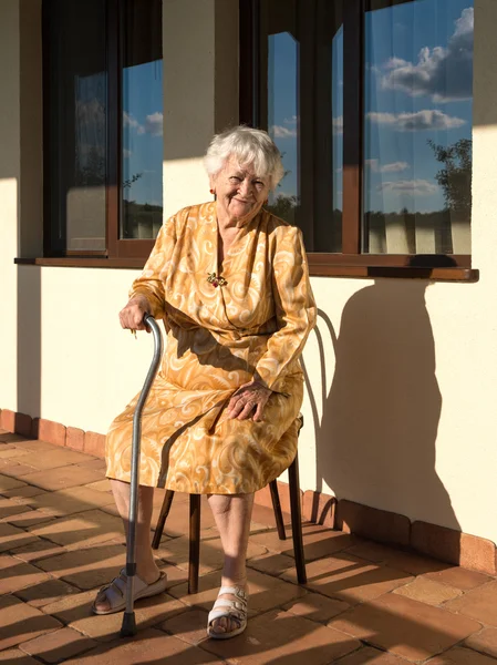 Vieille femme souriante assise près de la maison — Photo