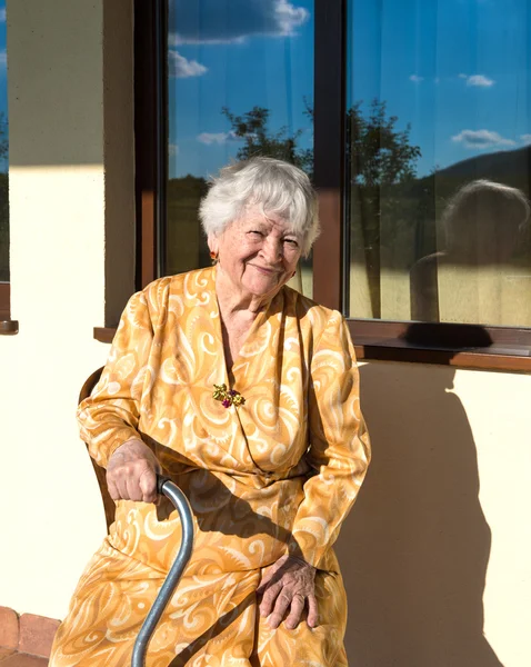 Evin oturan yaşlı kadın gülümsüyor — Stok fotoğraf